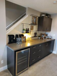 Under-stairs bar with dark cabinetry and beverage fridge